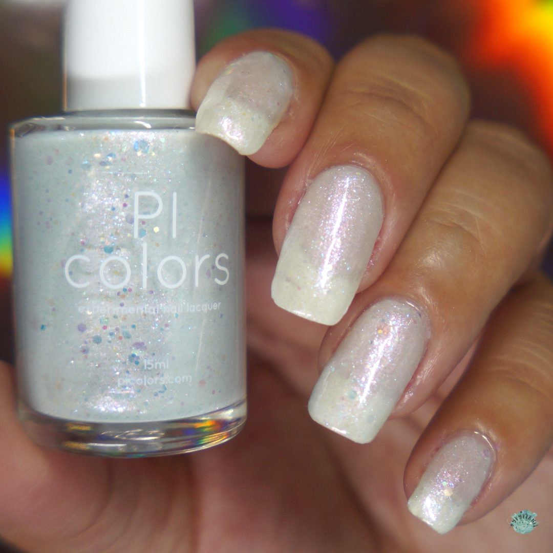 A hand showcases nails adorned with a shimmery, iridescent white crelly polish. The bottle of handmade nail polish, labeled "Troth of Innocence.001 White Nail Polish" by PI Colors, is held beside the nails, highlighting subtle flecks of glitter that catch the light.