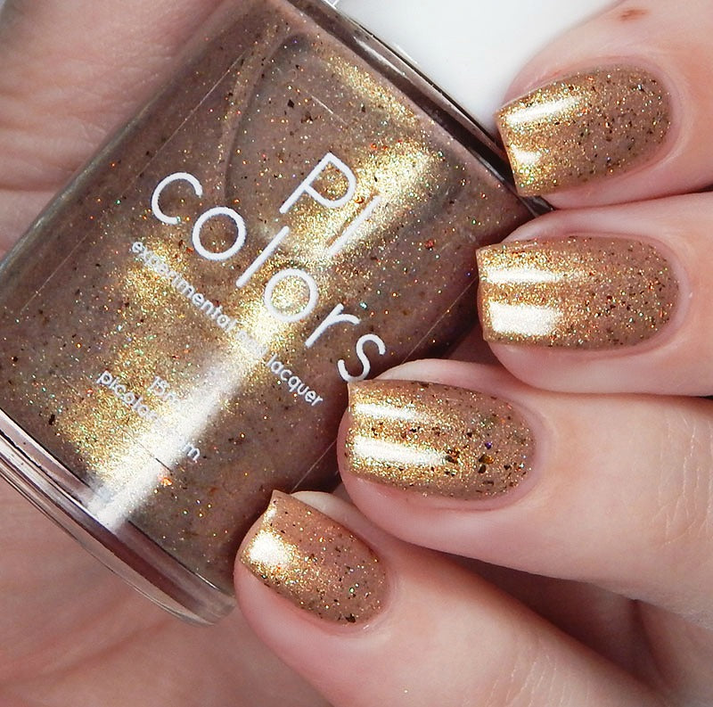 A close-up of a hand with neatly painted nails in a shimmering bronze hue, enhanced with holographic glitter. The hand holds a bottle of "Golden King.001 Gold Nail Polish" by PI Colors, displaying its luxurious glittery finish that beautifully catches the light.