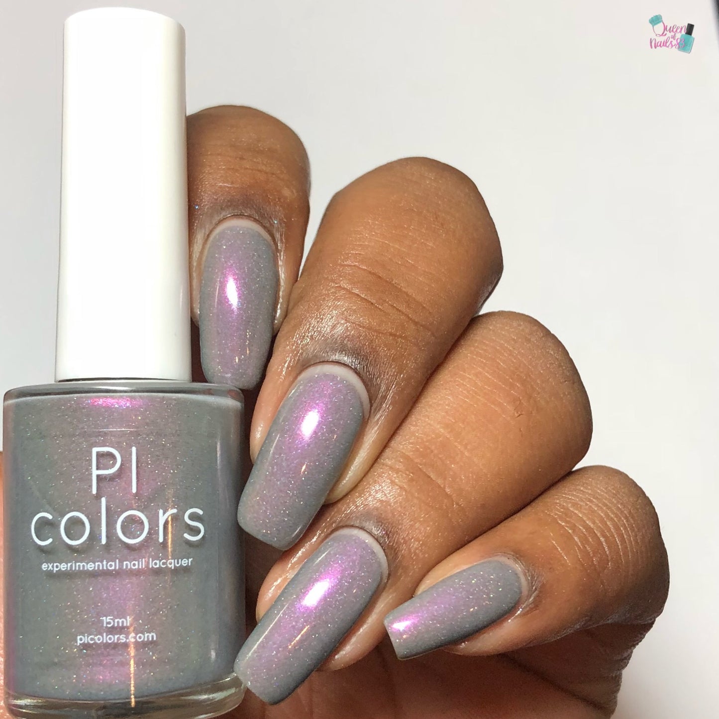 A close-up of a hand showcasing long nails adorned with Cirrus.118 Pink Gray Nail Polish, exhibiting a pink and purple shimmer. Nestled between the fingers, the nail polish bottle prominently displays "PI Colors" with "experimental 10-free lacquer" inscribed below.