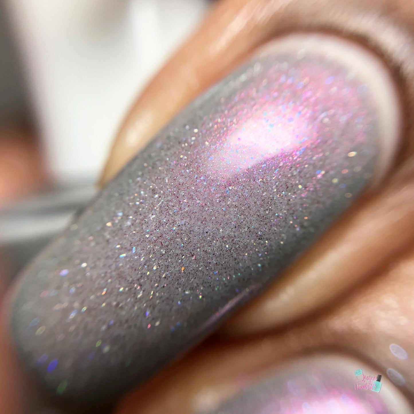 Close-up of a fingernail painted with PI Colors' Cirrus.118 Pink Gray Nail Polish, highlighting its gray base blended with iridescent pink and purple shimmer. The 10-free formula features fine glitter particles, adding a sparkling effect.