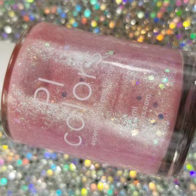 A bottle of PI Colors Pink Candy.210 Pink Nail Polish shimmers with silver glitter. It sits on a vibrant bed of sparkling confetti, accentuating the pastel pink jelly hue of the nail polish.