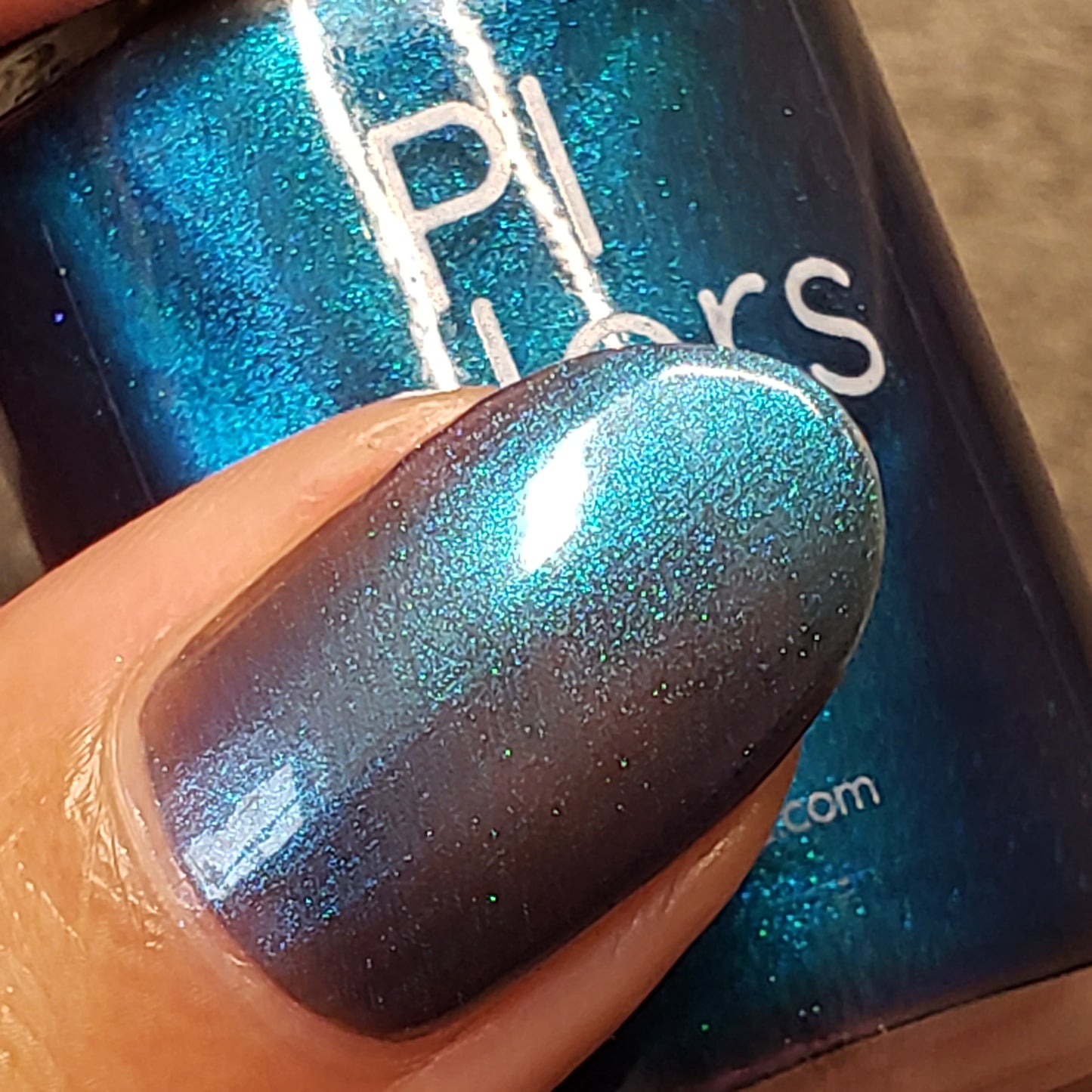 Close-up of a fingernail painted with Aurora Blue.316 by PI Colors, a luxurious nail lacquer that shimmers between blue and purple shades. This handmade nail polish is showcased next to its matching bottle, highlighting its stunning color shift in the light.