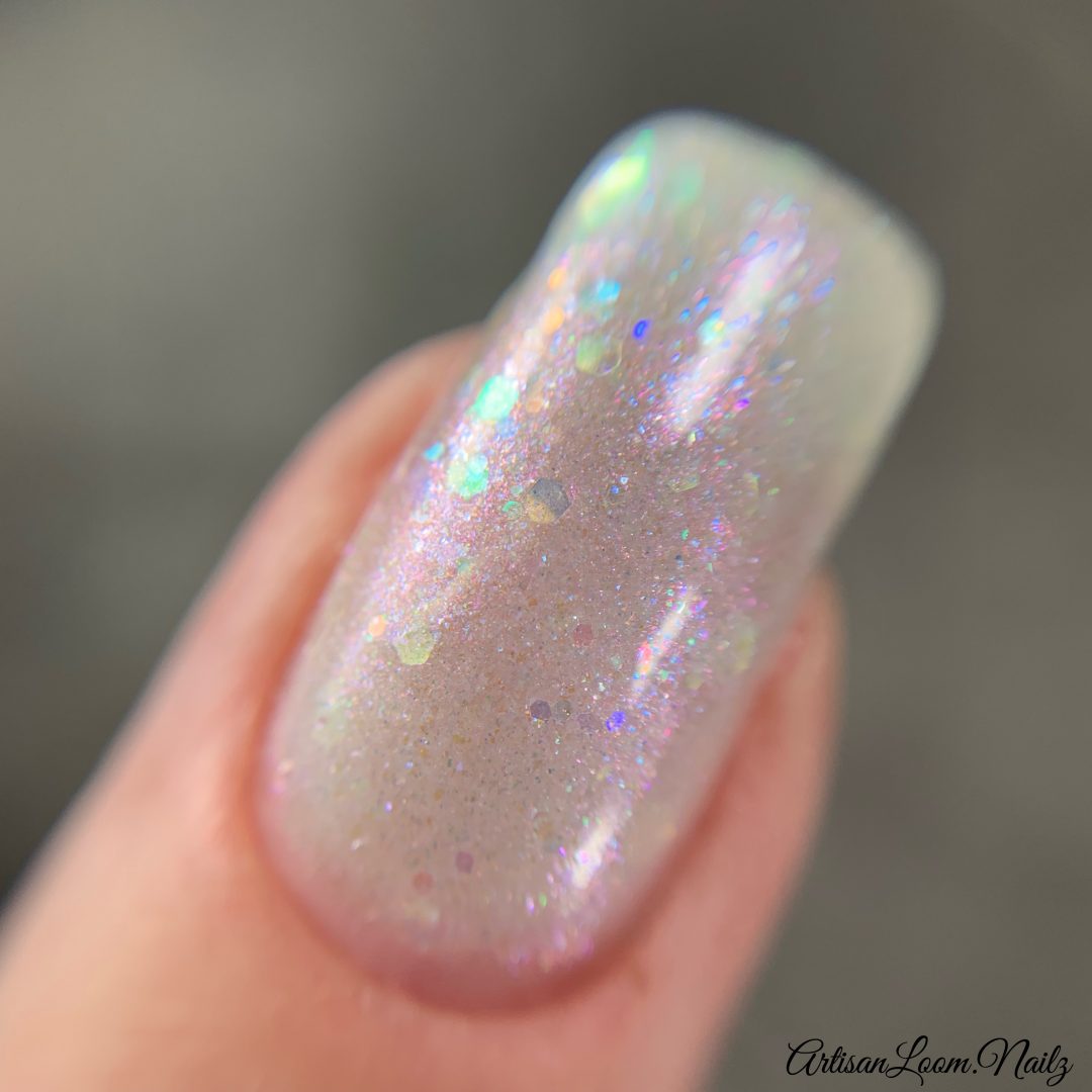 A close-up of a fingernail adorned with Troth of Innocence.001 White Nail Polish by PI Colors showcases the sheer, handmade formula with iridescent flakies. The nail exhibits a glossy, holographic effect, sparkling with multi-colored reflections and an array of pastel shades.