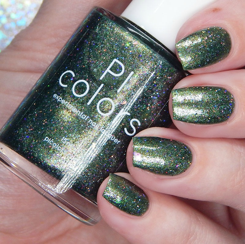 Close-up of a hand with sparkling deep green polish adorned with iridescent flakes. The bottle held is labeled "Phasers on Stun.078 Green Nail Polish" by PI Colors. The polish is glossy with multicolored glitter, reflecting light.
