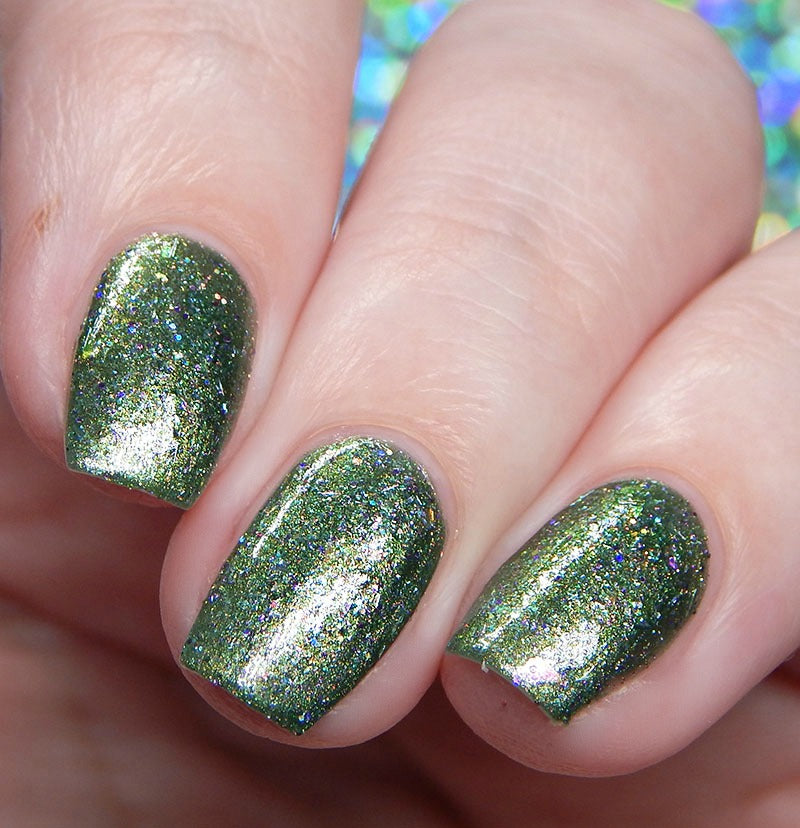 A close-up image showcases a hand with nails painted using PI Colors' Phasers on Stun.078 Green Nail Polish. The polish boasts a deep green hue with holographic glitter, giving the nails a well-manicured, glossy finish adorned with multicolored sparkles for an enchanting effect.
