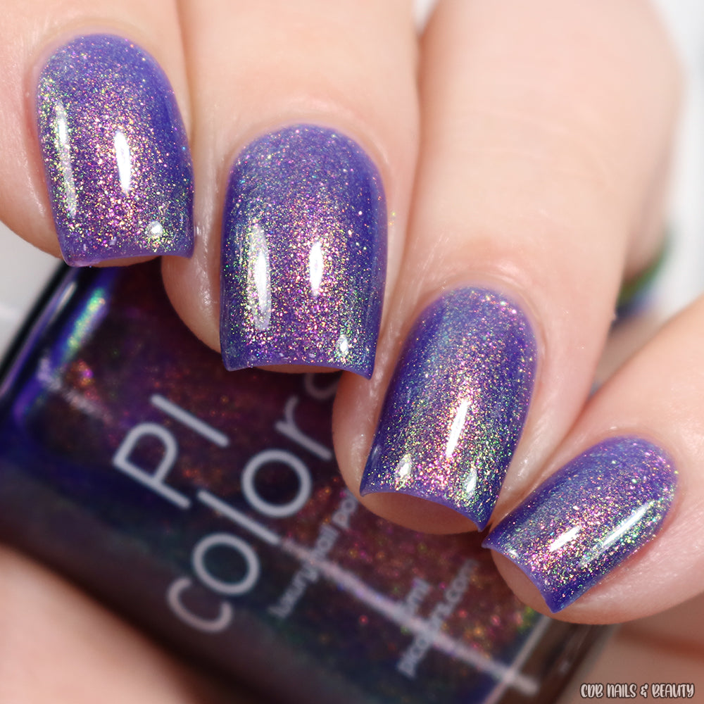 Close-up of a hand with nails painted in a shimmering violet purple hue featuring holographic glitter. The fingers are holding a bottle of PI Colors' 90s Kind of World Purple Nail Polish, showcasing the vibrant, sparkling effect and delicate aurora pigment on the nails.