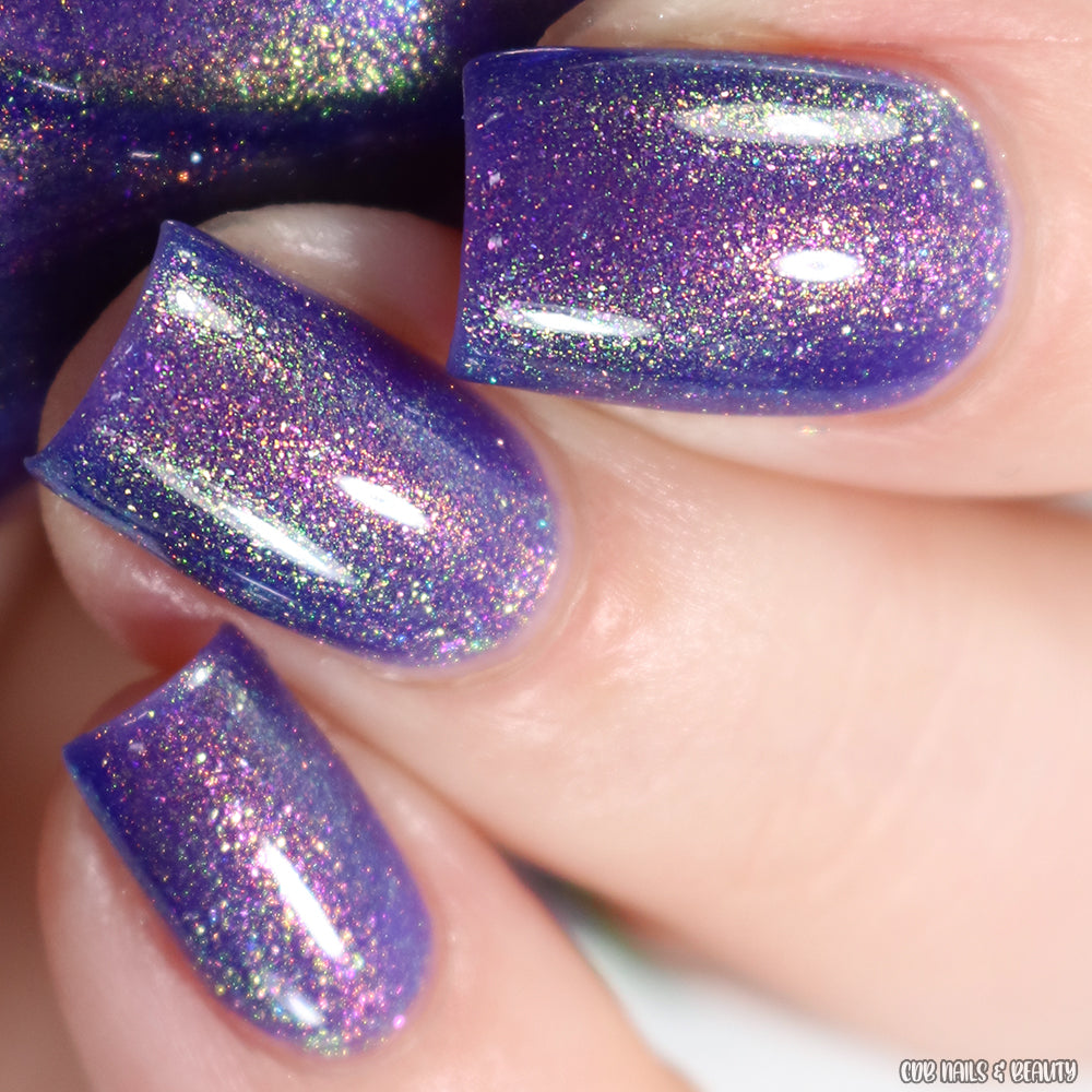 Close-up of nails adorned with a vibrant, handmade violet polish called "90s Kind of World Purple Nail Polish" by PI Colors. The aurora pigment imbues the nails with a sparkling, color-shifting effect that reveals subtle hints of pink and green. They are neatly manicured and boast a glossy finish.