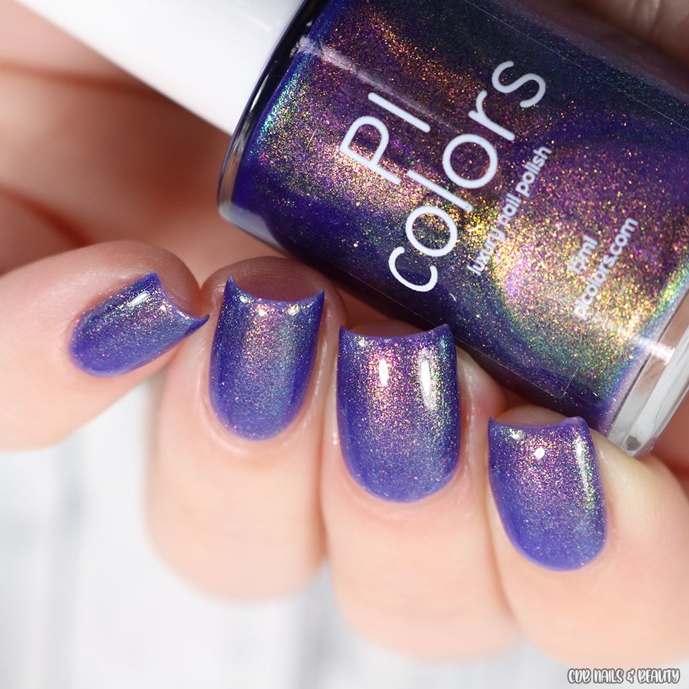 A hand displays impeccably manicured nails adorned in a glossy violet purple polish. The PI Colors bottle, labeled "90s Kind of World Purple Nail Polish," is enhanced with an aurora pigment that captivates with its enchanting blend of purple, blue, and gold hues.