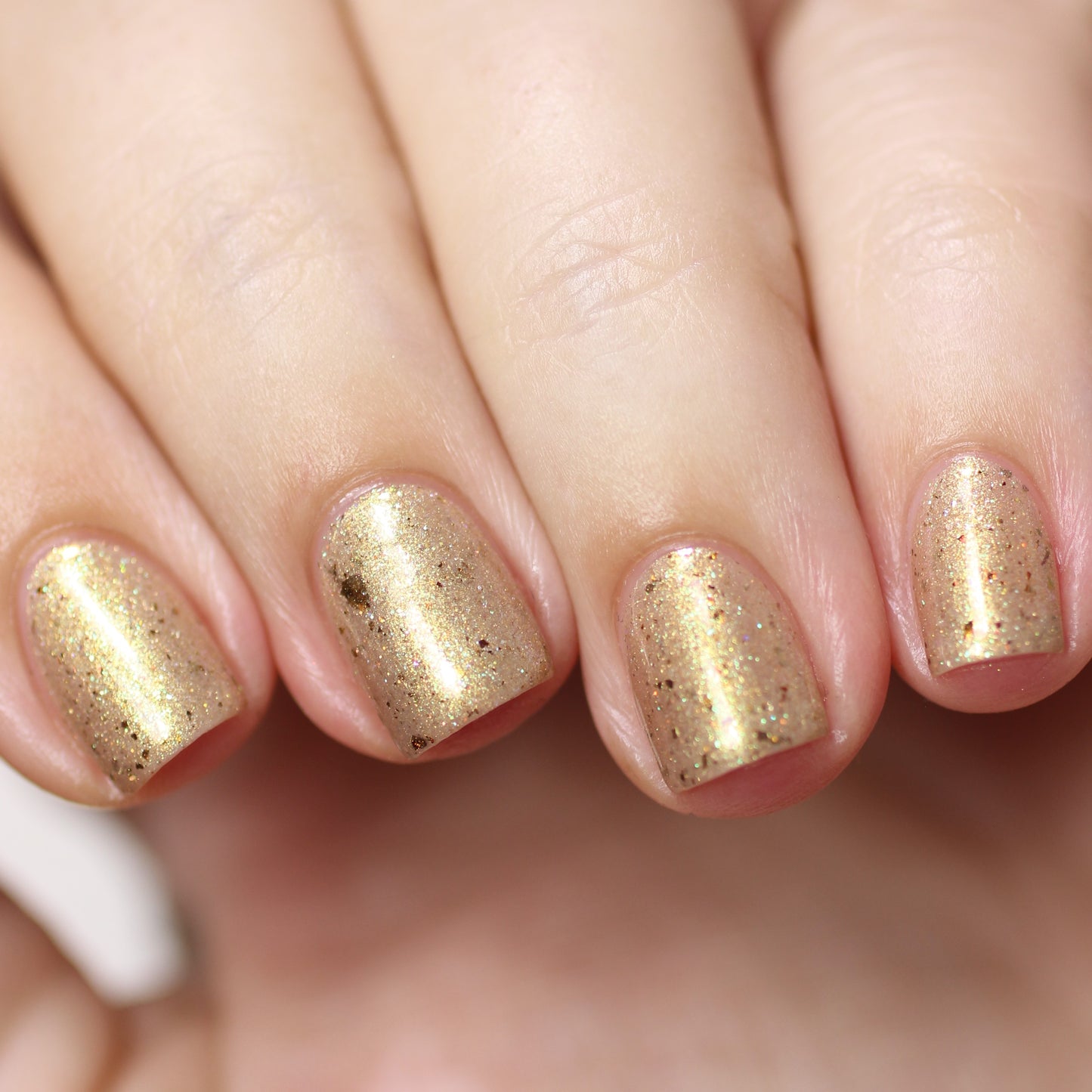 Close-up of a hand with fingers showcasing nails adorned in Golden King.001 Gold Nail Polish by PI Colors. The shimmery lacquer, infused with holographic glitter, captures light and enhances the shine. The softly blurred background accentuates the elegance.