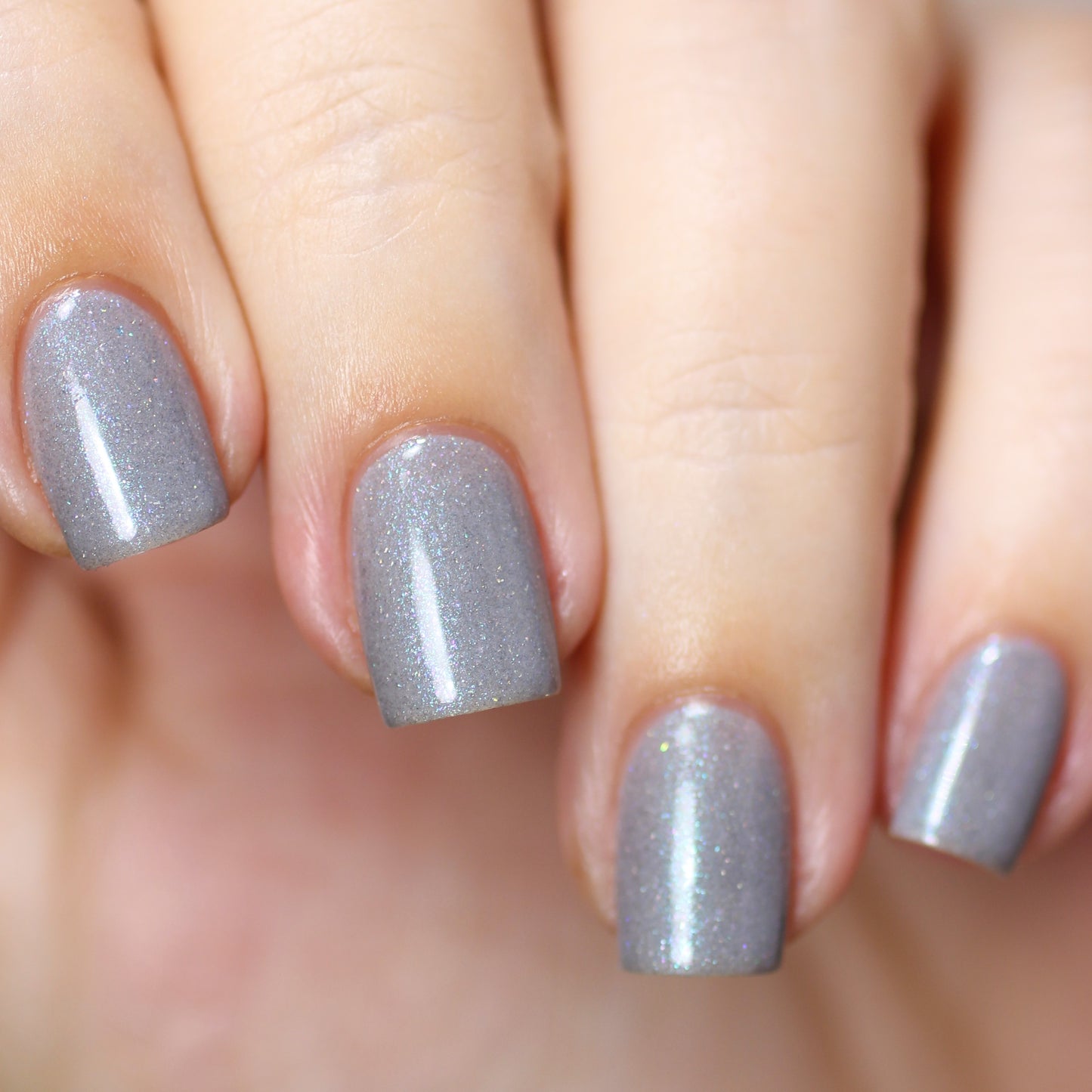 Close-up of a hand with neatly manicured nails painted in PI Colors Asperitas.105 Blue Gray Nail Polish. The nails are short and evenly shaped, showcasing a smooth, glossy finish with a subtle holographic sparkle.