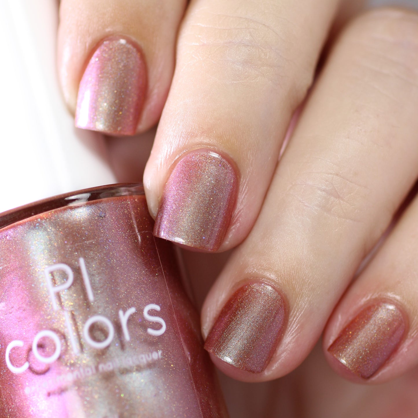 Close-up of a hand with short nails painted in the luxurious shade "Beta Ceti.055" which is a rust orange red nail polish. The nail polish bottle is held next to the fingers, featuring the text "PI Colors" and showcasing the vibrant polish in the same shade.