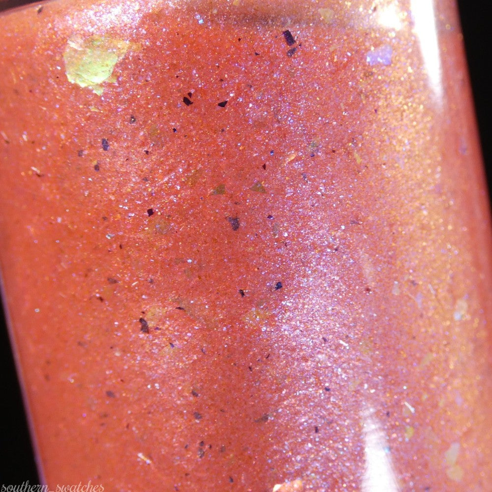 Close-up of Lala Ngoxolo Kumkani Coral Nail Polish, a custom handmade creation from PI Colors, featuring multicolored glitter flecks. The light dances off the surface, highlighting iridescent rainbow flakes and its glossy texture.