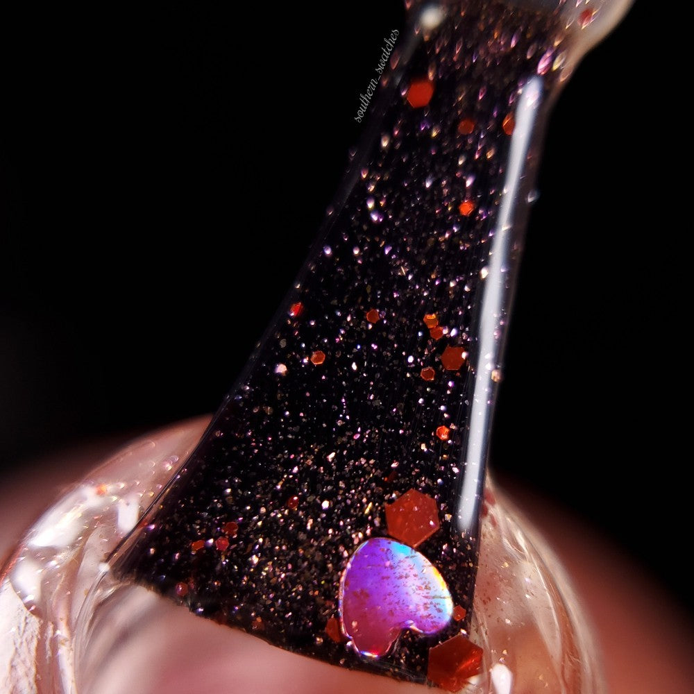A close-up of the PI Colors Strawberry Heart.208 Red Nail Polish Topper brush coated with black polish, shimmering with glitter and holographic hearts. The topper sparkles with red, pink, and purple highlights against a dark background.