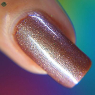 Close-up of a fingernail featuring PI Colors' Beta Ceti.055 Rust Orange Red Nail Polish, showcasing a glossy, multichrome shimmer with metallic purple tones that create a gradient effect. The background features a blurred blend of green, blue, and purple hues.