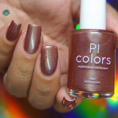 A close-up captures a hand with fingers adorned in a shimmering bronze multichrome polish. The hand clutches a bottle of PI Colors Beta Ceti.055 Rust Orange Red nail lacquer, highlighting the same exquisite bronze hue against a vibrant, colorful backdrop.