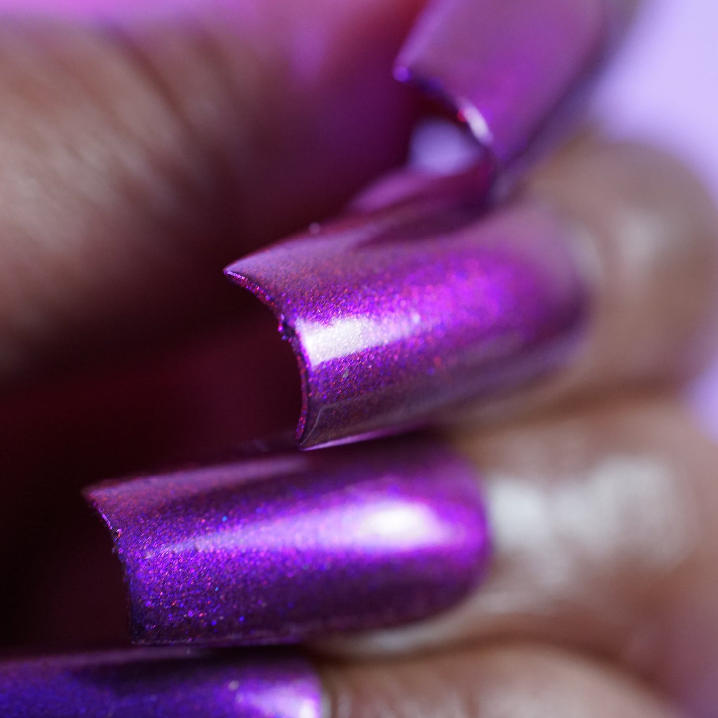 A close-up showcases a hand with PI Colors' "Danbury Does It.000," featuring metallic purple multichrome on long, slightly chipped nails. The vibrant, luxurious texture of this exquisite 10-free polish shimmers against the blurred background.