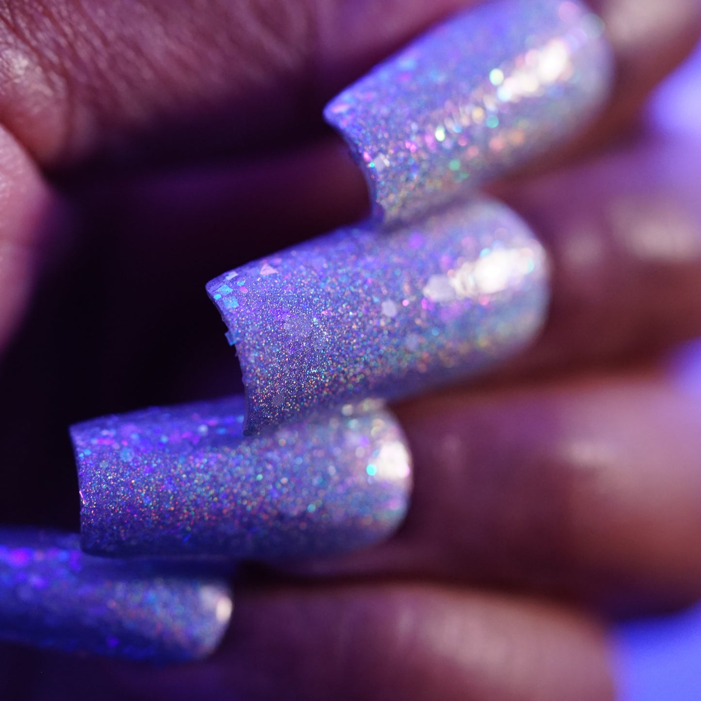 Close-up of a hand with purple glittery nail polish on a blurred background