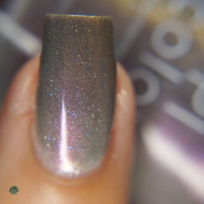 A close-up of a fingernail adorned with Cirrus.118 Pink Gray Nail Polish by PI Colors, reflecting light with delicate hints of pink and purple shimmer. The texture is smooth with a subtle sparkle, while the blurred background keeps the focus on this elegant display.