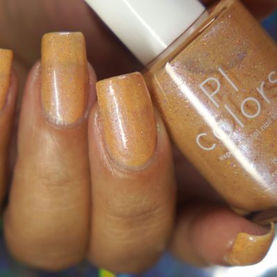 A close-up of a hand with nails coated in the shimmery pale orange hue of Sunrise Tellin.027 nail polish captures attention, as it holds a bottle adorned with the PI Colors label. The polish sparkles beautifully, enhanced by a touch of holographic glitter.
