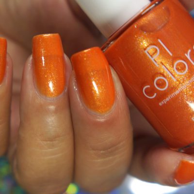 A hand showcases neatly manicured nails adorned with the vibrant, shimmery hue of Sun Conure.097 Orange Nail Polish. A bottle of this luxurious nail lacquer is held between the fingers, labeled with "PI Colors," displaying visible reflections on its glossy surface.