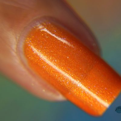 A close-up showcases a fingernail adorned with PI Colors' Sun Conure.097 Orange Nail Polish, exhibiting a smooth and reflective finish with a subtle shimmer. This luxury nail lacquer draws attention in the blurred background, accentuating its vibrant color and texture.