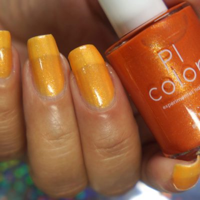 A close-up of a hand with nails painted in a vibrant, shimmery orange-yellow hue is seen holding a bottle of PI Colors' "Sun Conure.097 Orange Nail Polish." The background showcases a subtle iridescent pattern, amplifying the allure of these luxury nail lacquers.