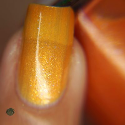 A close-up of a fingernail adorned with PI Colors' Sun Conure.097 Orange Nail Polish showcases its shimmering beauty, capturing the light for a glossy finish. In the background, you can see part of the elegant orange nail polish bottle, enticing those in search of premium 10-free polishes.