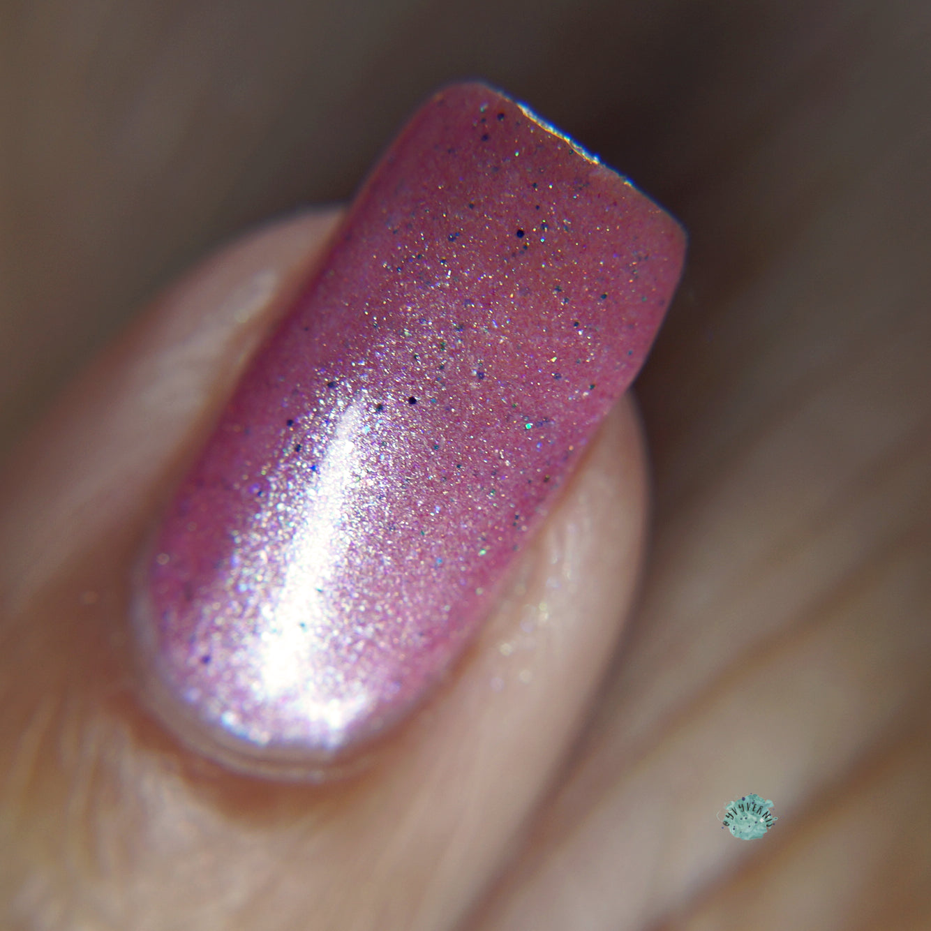 A close-up of a fingernail adorned with PI Colors' Roseate Bliss.012 Pink Nail Polish, showcasing delicate specks of black and subtle holographic glitters. The nail is impeccably manicured, with the surrounding skin smooth and flawless.