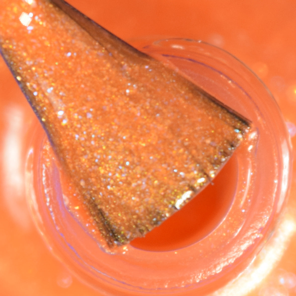 Close-up of a nail polish brush dipped in a bottle of Sun Conure.097 Orange Nail Polish by PI Colors. This luxury 10-free lacquer boasts a glittery texture and appears vibrant and glossy.