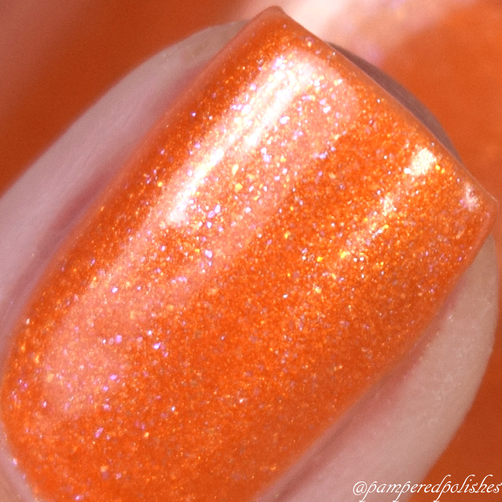 Close-up of a fingernail painted with the vibrant Sun Conure.097 Orange Nail Polish by PI Colors. The 10-free polish sparkles under the light, showcasing a mix of fine glitter and a glossy finish.