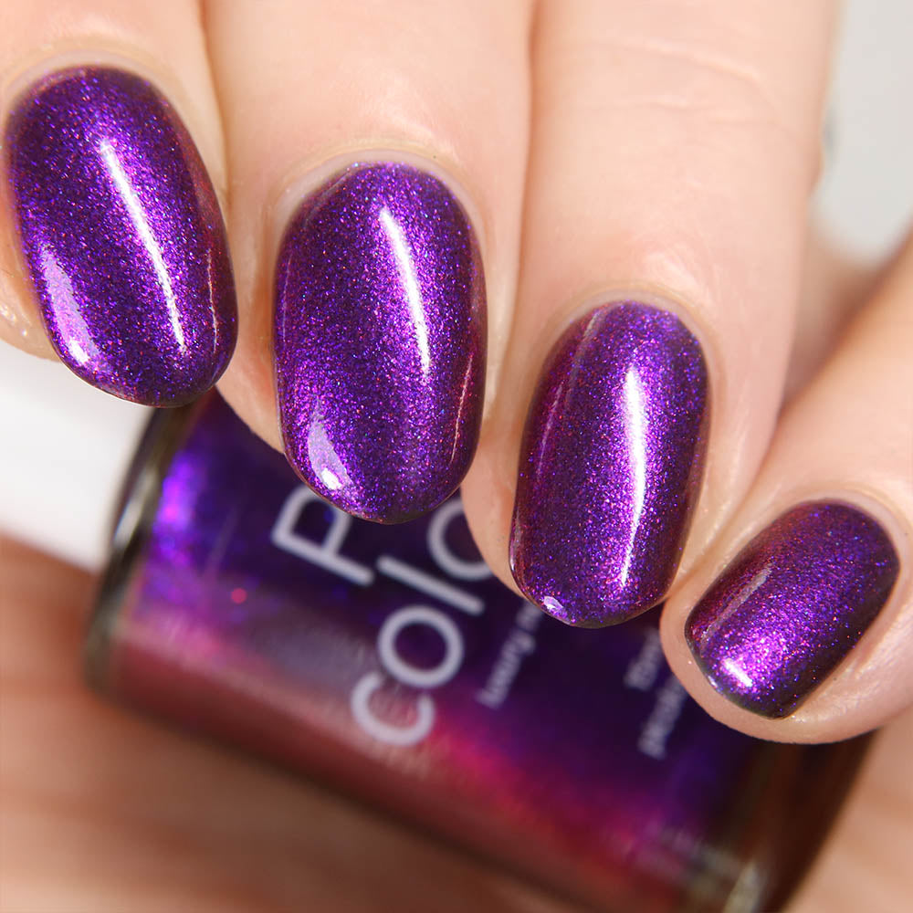 Close-up of fingers with PI Colors' "Danbury Does It.000" shimmering purple multichrome nail polish. The glossy finish and fine glitter create a sparkling effect, alongside a matching partially visible bottle in the background.