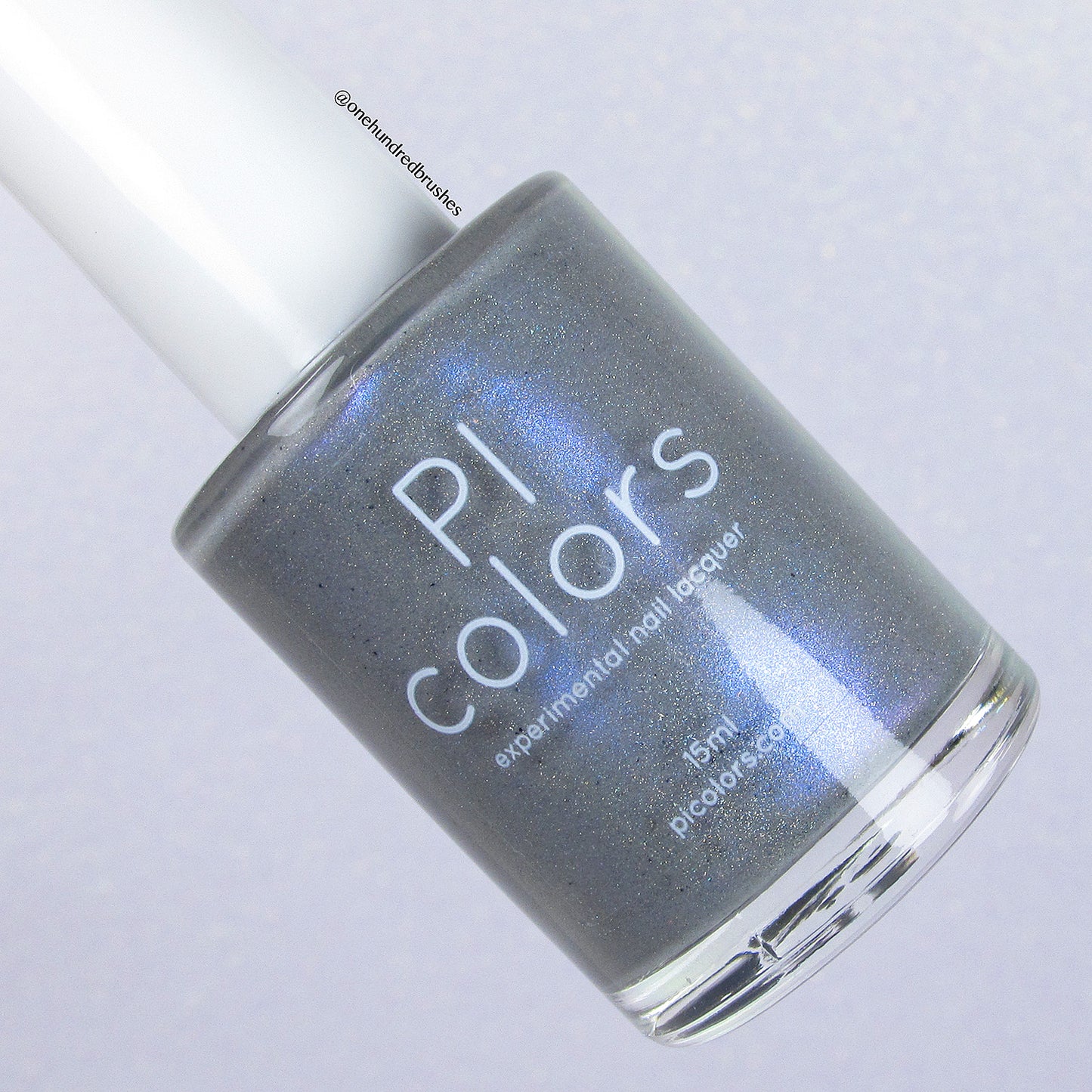 A bottle of Draco.055 Blue Gray Nail Polish by PI Colors, offering a shimmering slate gray hue with a touch of blue and delicate holographic glitter. The bottle is topped with a white cap, and the brand name along with product details are elegantly printed on the glass against a subtle, neutral backdrop.