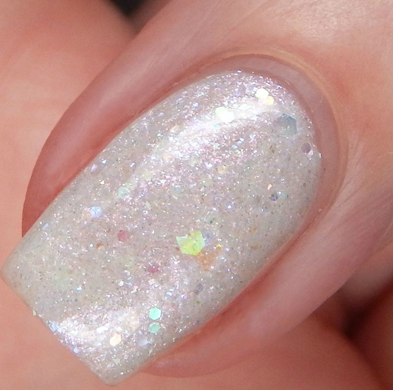 Close-up of a fingernail adorned with PI Colors' Troth of Innocence.001 White Nail Polish, featuring captivating iridescent glitter and flakies. The polish shimmers in a spectrum of hues atop a light, pearlescent base coat. The edges of the nail are expertly manicured.