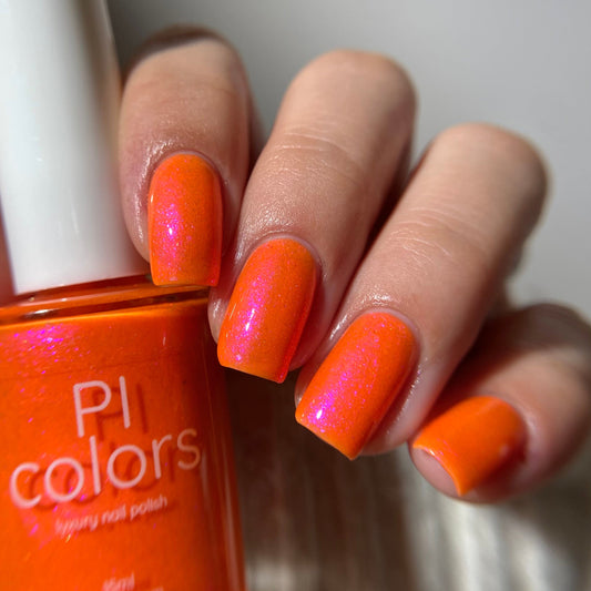 Hand with orange nail polish holding a bottle of PI Colors nail polish.