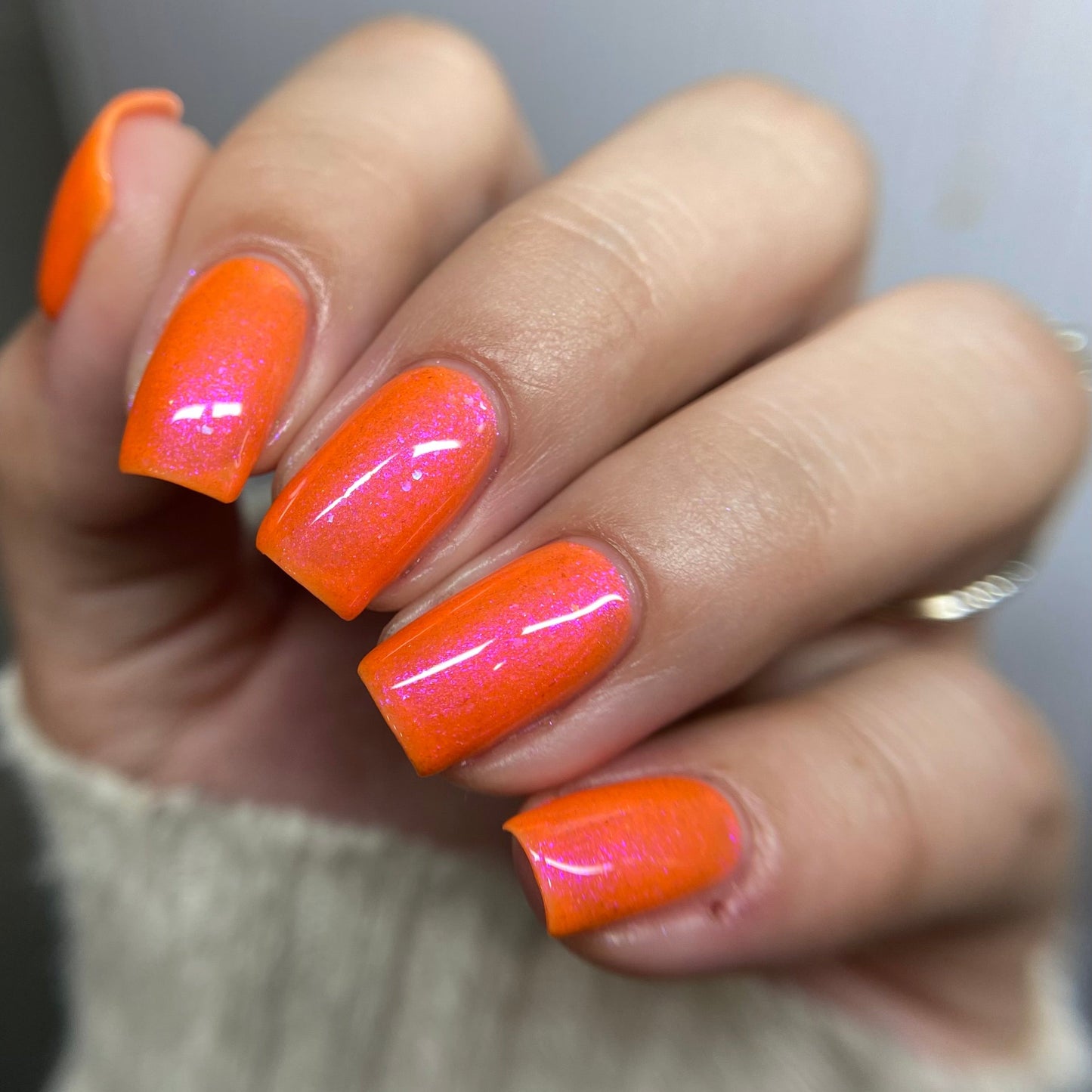 Hand with bright orange nail polish on a neutral background
