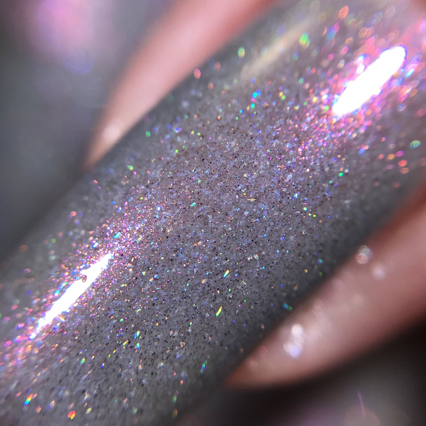 A close-up of a fingernail showcases the 10-free Cirrus.118 Pink Gray Nail Polish by PI Colors, highlighting its shimmery, silver-gray finish that reflects pink and rainbow lights for a smooth and glittery texture under bright lighting.