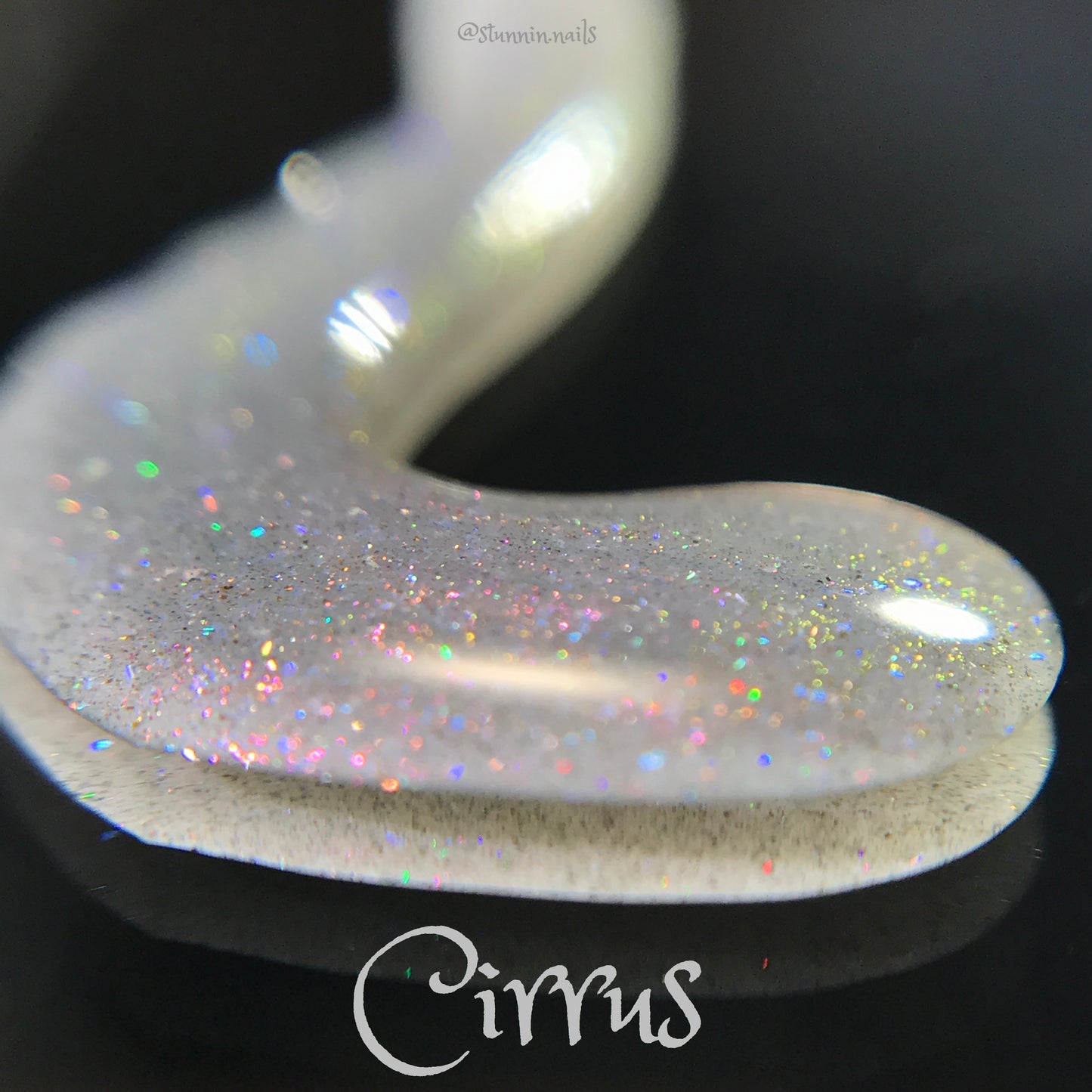 A close-up of the Cirrus.118 Pink Gray Nail Polish by PI Colors showcases a mesmerizing swirl on a black surface. Featuring a gray-based polish with a pearlescent white foundation adorned with colorful glitter and subtle purple shimmer, it reflects light beautifully. An ideal choice for those who appreciate 10-free beauty products.