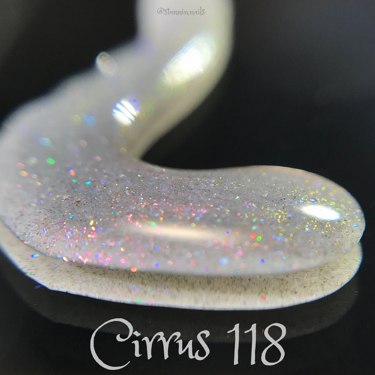 A close-up of PI Colors' Cirrus.118 Pink Gray Nail Polish swatch reveals a gray base with a shimmery, iridescent finish adorned with tiny rainbow specks. The name "Cirrus 118" is elegantly displayed alongside part of a curved brush stroke, set against a dark background and highlighted by a subtle purple shimmer.