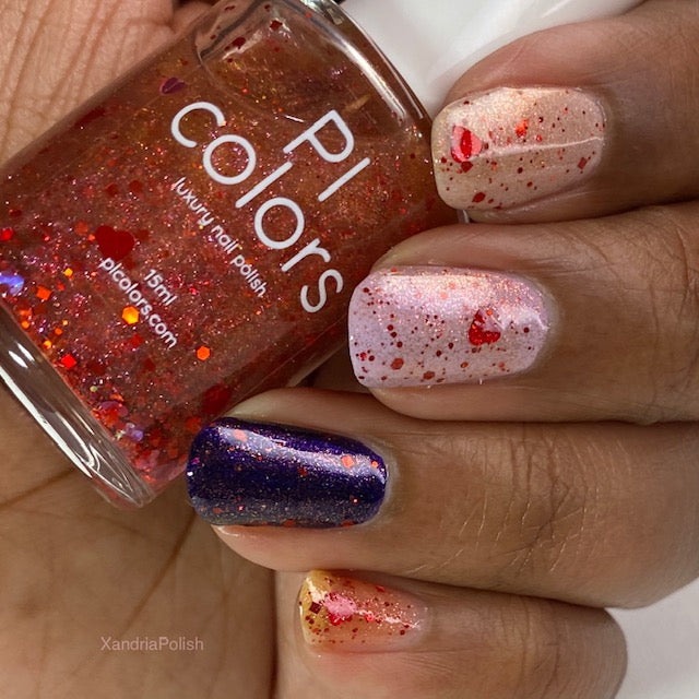 With a colorful and vibrant display of nail artistry, a hand features PI Colors' 10-free nail polish collection: the thumb sparkles with Strawberry Heart.208 Red Nail Polish Topper, the index and middle fingers are adorned with a pale pink base speckled with this same red glitter topper, the ring finger is bedazzled in dark blue glitter accented by holographic hearts, while the pinky showcases a pale yellow hue enhanced by red speckles from the Strawberry Heart.208 topper.
