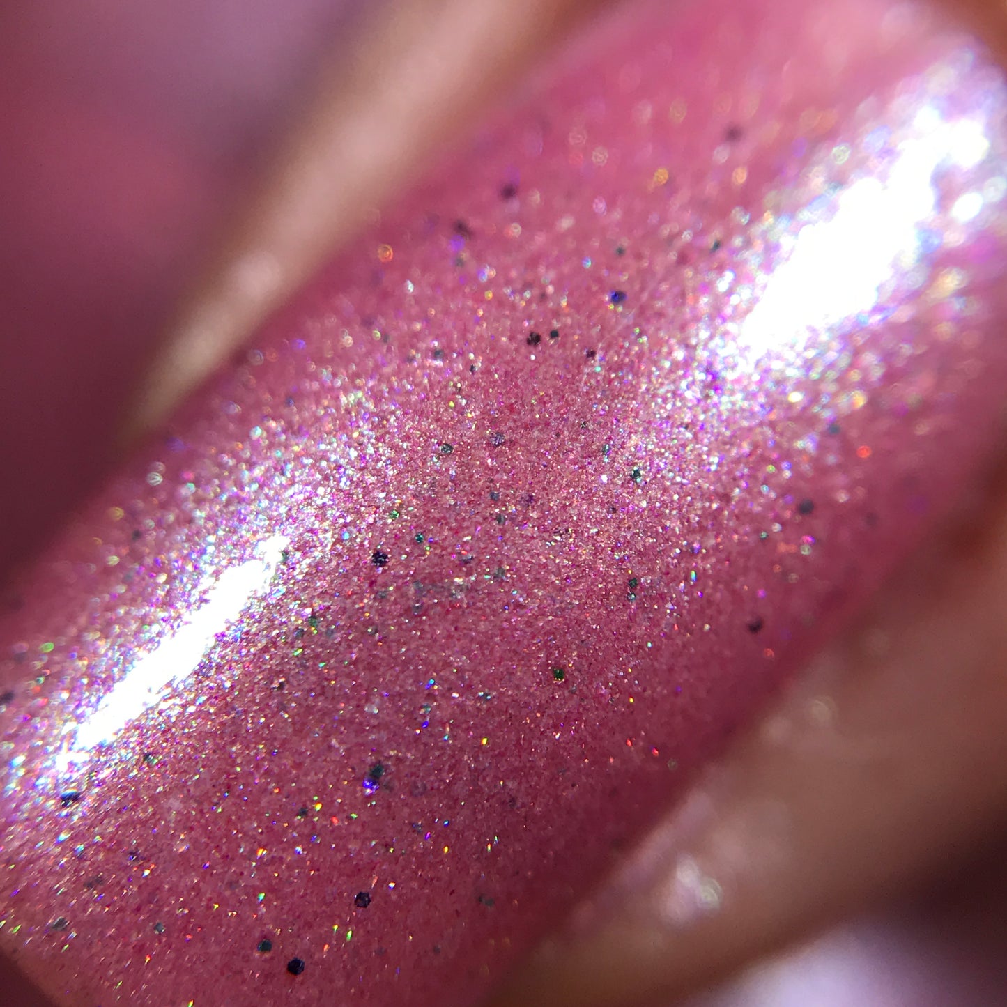 A close-up reveals a fingernail coated in PI Colors' Roseate Bliss.012 Pink Nail Polish, highlighted by intricate holographic glitters. The glossy surface captures and reflects light beautifully, creating an enchanting effect.
