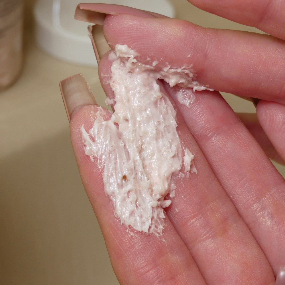 Fingers with long, painted nails delicately hold a small amount of PI Colors' Strawberry Whipped Soap Sugar Scrub, showcasing its thick, creamy texture that suggests an exfoliating benefit, against a neutral backdrop.