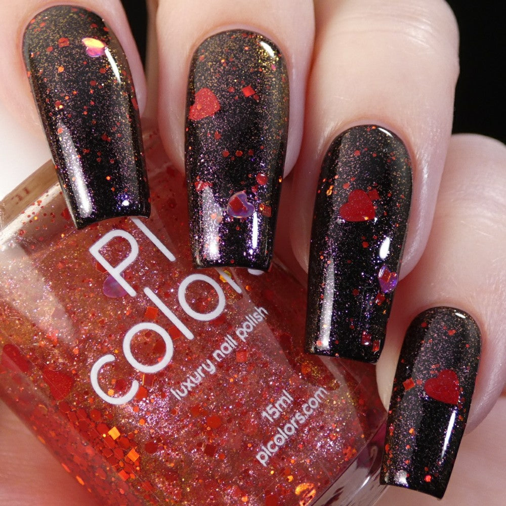 Close-up of a hand with long nails painted in glossy black, complemented by holographic hearts featuring red and orange glitter. The hand holds the PI Colors Strawberry Heart.208 Red Nail Polish Topper, displayed in a transparent bottle infused with red glitter.