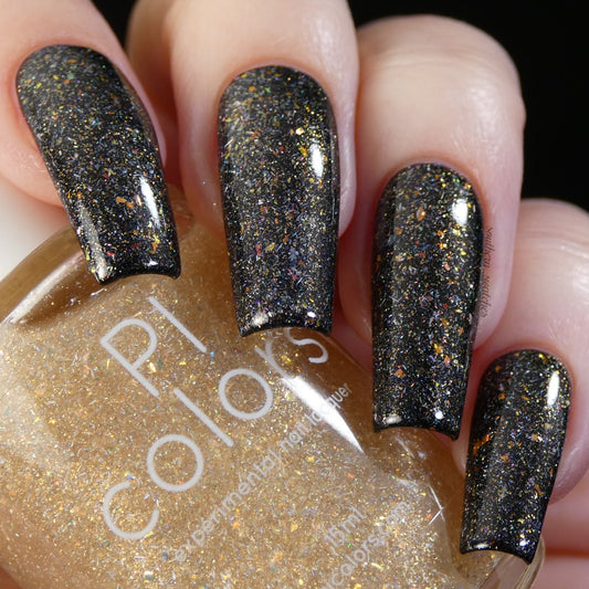 A close-up shows a hand with long nails painted in black nail polish, enhanced by color-shifting flakes and multicolored sparkles. Nestled between the fingers is a partially visible bottle of PI Colors' "Honey Bee" .060 Gold Nail Polish Topper, contributing an elegant golden touch.