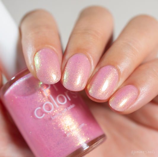 A hand with neatly manicured nails painted in PI Colors’ Lemon Pink Sugar Cookie.422, a luxury nail lacquer featuring an iridescent, shimmering light pink finish that catches the light beautifully, holding the matching bottle.