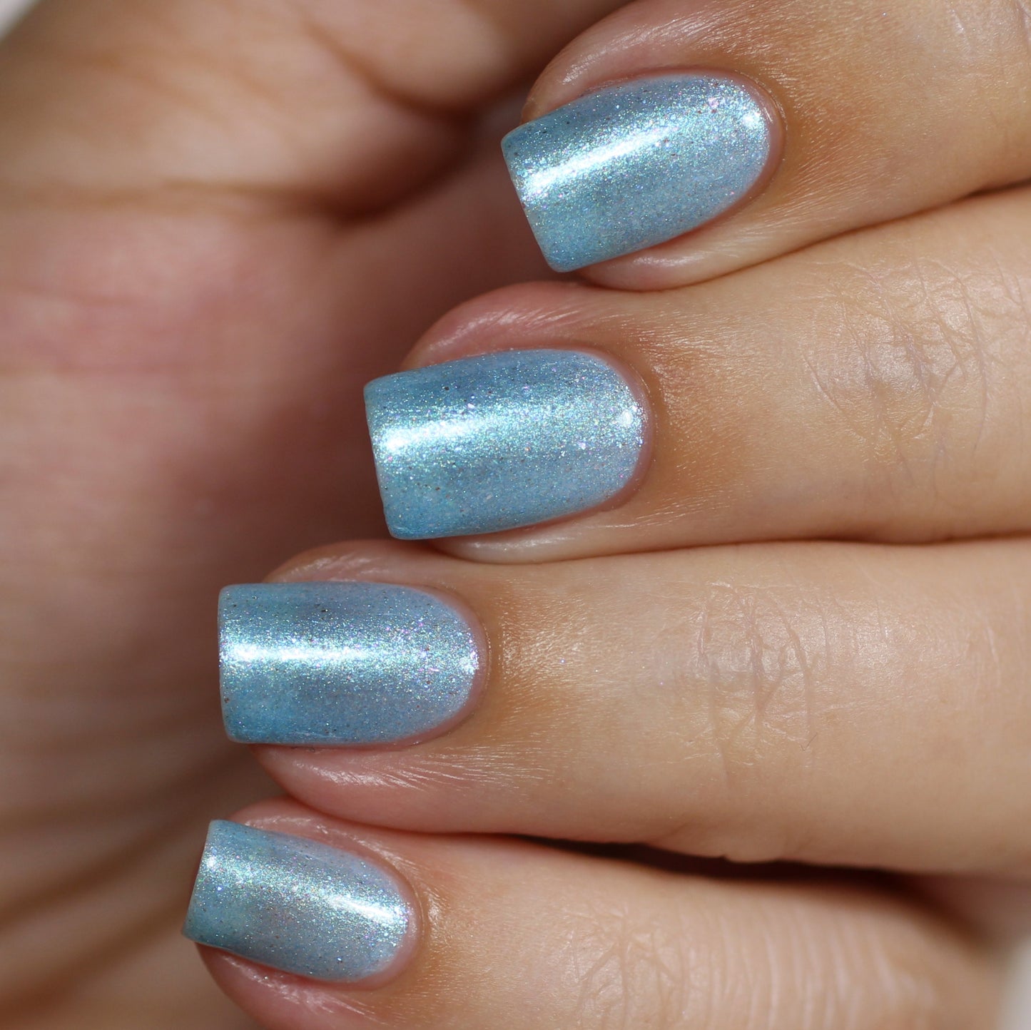Close-up of a hand with nails painted in PI Colors' Loulaki.101 Blue Nail Polish, a shimmery light blue handmade polish featuring iridescent flakies.