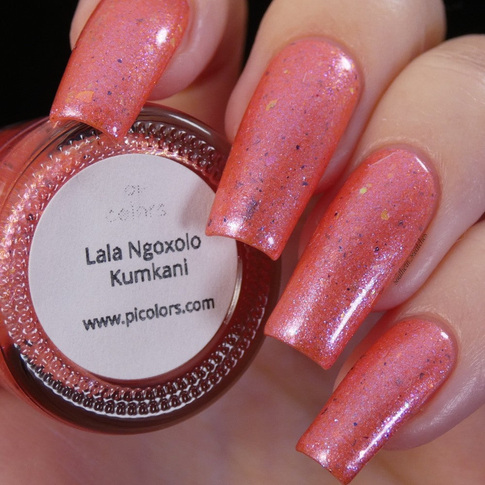 A close-up captures a person's hand showcasing long, glossy pink nails embellished with iridescent rainbow flakes. Next to it, the nail polish bottle cap displays "Lala Ngoxolo Kumkani Coral Nail Polish" and "www.picolors.com". This custom handmade creation by PI Colors adds a speckled shimmer finish.