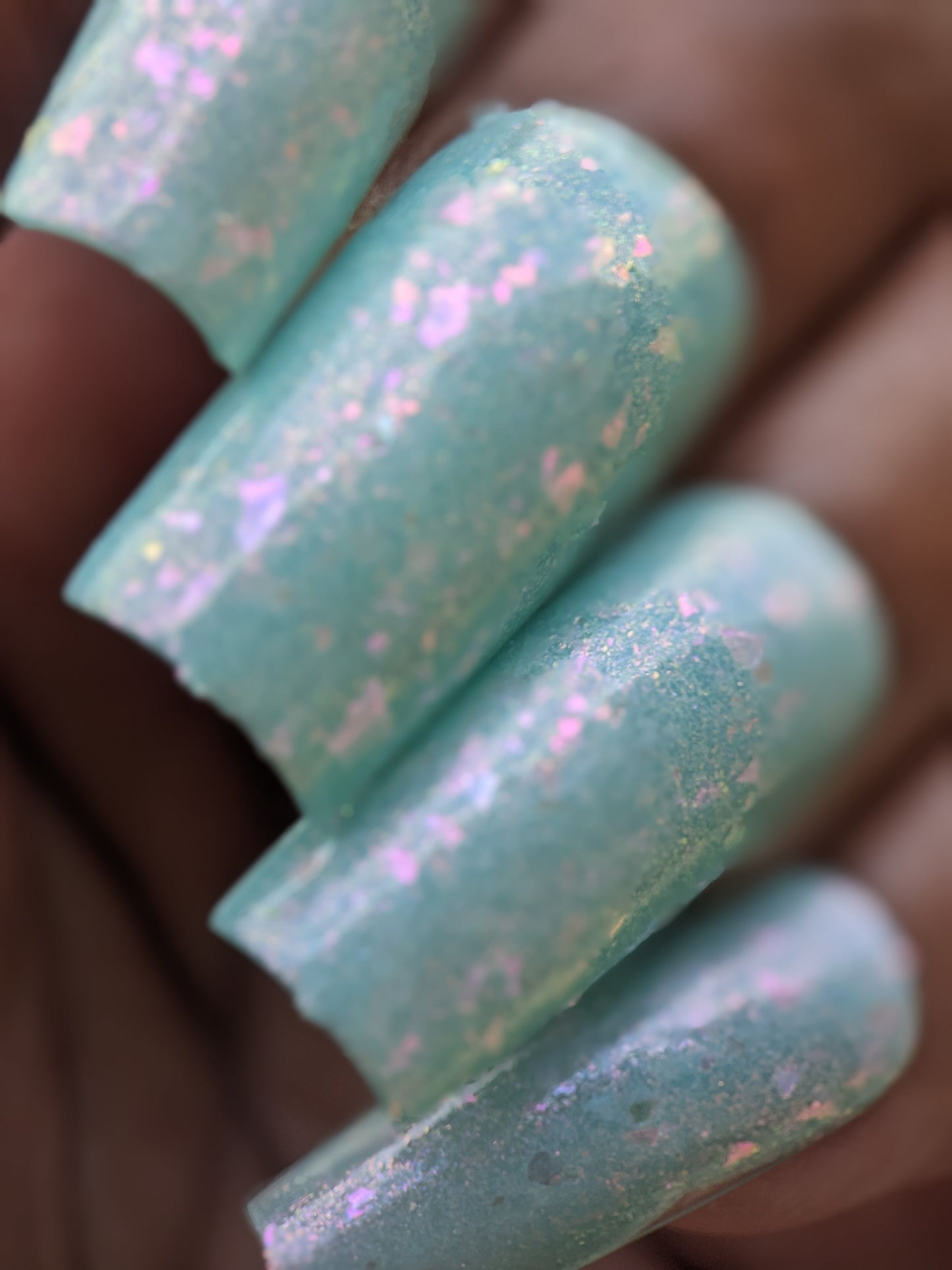 Close-up of manicured nails with PI Colors' shimmering pastel teal polish, "Star of Siam.000." This 10-free nail polish showcases colorshifting rainbow flakies that catch the light, creating a textured and sparkling effect.