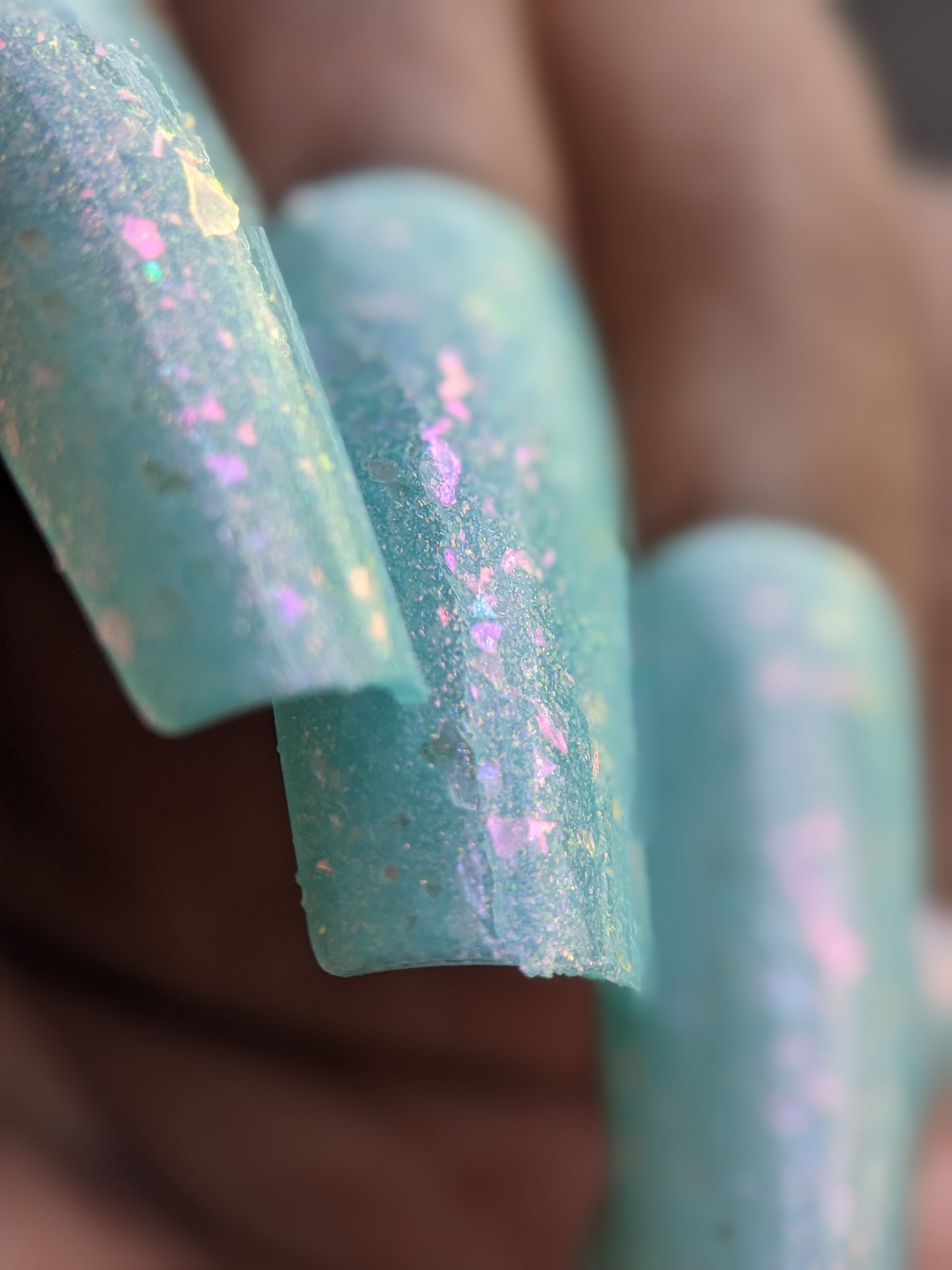 Close-up of long, rectangular fingernails painted with Star of Siam.000 by PI Colors, a pastel teal nail polish infused with colorshifting rainbow flakies. The focus is on the intricate details and texture of this mesmerizing, 10-free nail art.