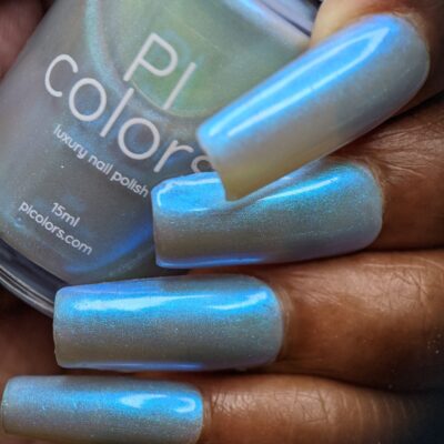 Close-up of a hand with long nails painted in "Cloud Rainbow.303 Blue Nail Polish," an electric silver blue shade from PI Colors. The nail lacquer bottle gleams beside them, showcasing a colorshift effect that gives the nails a glossy, shimmering finish.