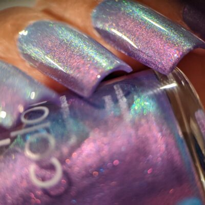 Close-up of fingernails featuring Dusk Rainbow.321 Purple Nail Polish by PI Colors, highlighting a deep purple shade with an iridescent finish. The polish blends hues of cyan and green, creating a shimmering, multicolor effect akin to an aurora shimmer.